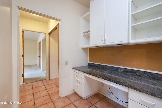 kitchen with light tile patterned floors, white cabinets, built in desk, and open shelves