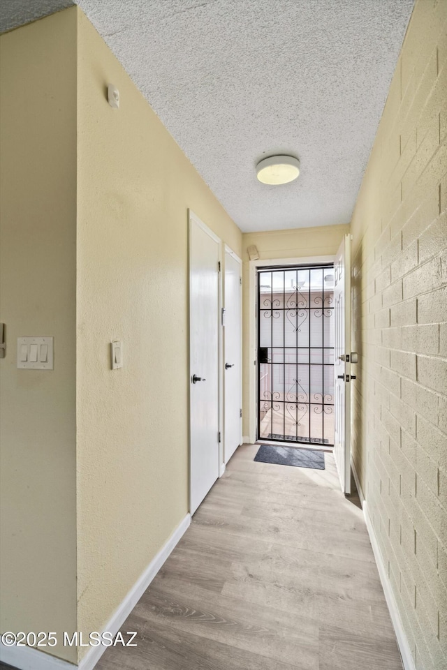 corridor with brick wall, a textured ceiling, and light wood-type flooring