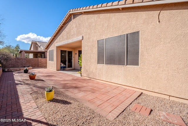 rear view of property with a patio, fence, and stucco siding