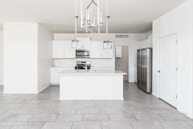 kitchen with stainless steel appliances, hanging light fixtures, white cabinets, and an island with sink