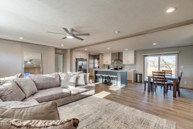 living room featuring a textured ceiling, crown molding, ceiling fan, and light hardwood / wood-style flooring