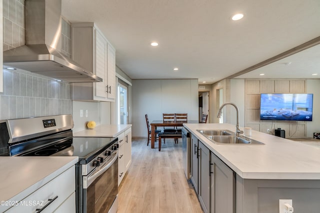 kitchen with appliances with stainless steel finishes, an island with sink, wall chimney range hood, sink, and white cabinetry