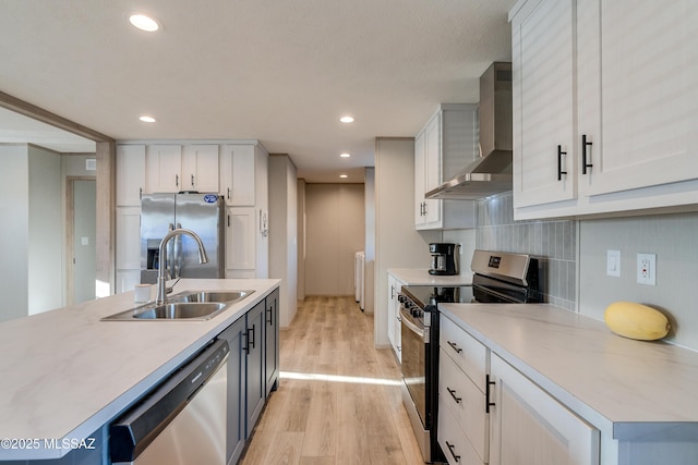 kitchen featuring white cabinetry, light wood-type flooring, sink, appliances with stainless steel finishes, and wall chimney exhaust hood