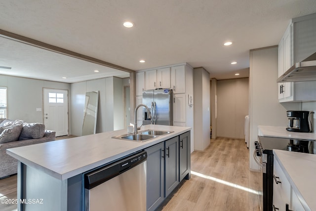 kitchen with sink, light wood-type flooring, stainless steel appliances, white cabinets, and a kitchen island with sink