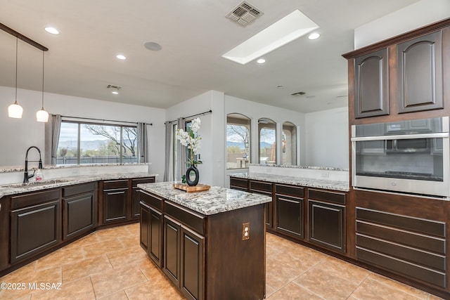 kitchen featuring a sink, visible vents, stainless steel oven, dark brown cabinets, and hanging light fixtures