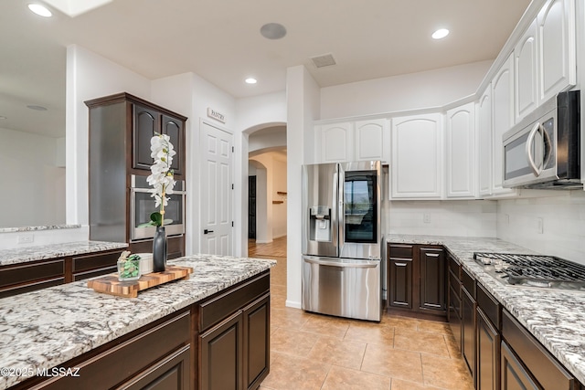 kitchen featuring arched walkways, stainless steel appliances, dark brown cabinets, and white cabinetry