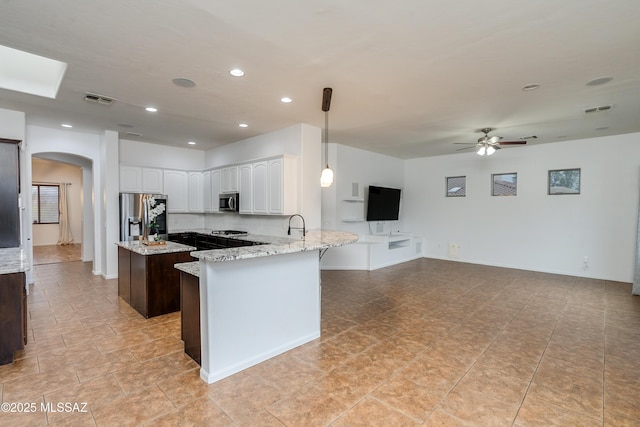 kitchen featuring light stone counters, arched walkways, appliances with stainless steel finishes, open floor plan, and white cabinetry