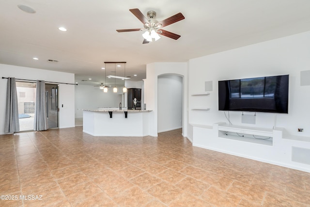 unfurnished living room with a ceiling fan, arched walkways, baseboards, and recessed lighting