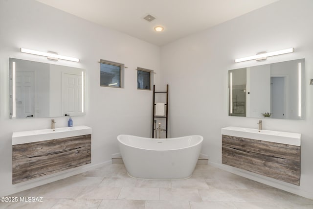 full bathroom featuring a freestanding bath, two vanities, a sink, and visible vents