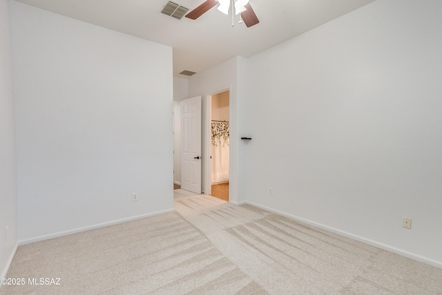 spare room with a ceiling fan, light colored carpet, visible vents, and baseboards