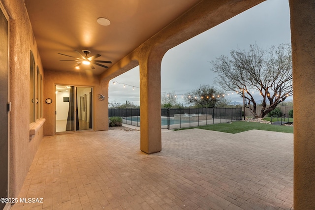 patio terrace at dusk with ceiling fan, a fenced backyard, and a fenced in pool