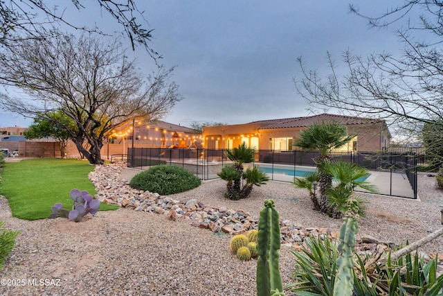 rear view of property featuring a yard, fence, a fenced in pool, and stucco siding