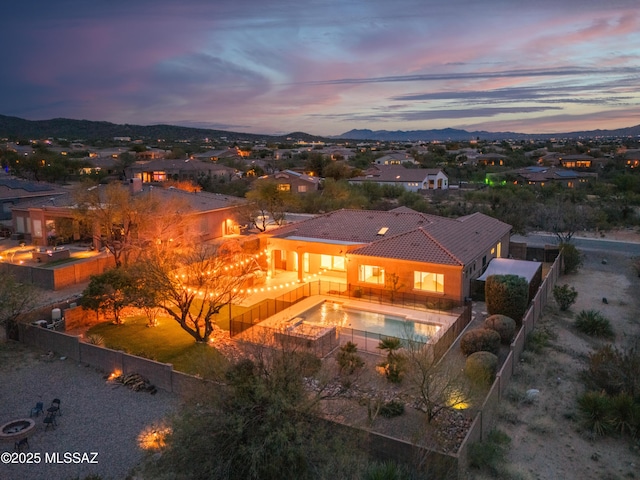 back of house at dusk featuring a fenced backyard, a tile roof, a residential view, and a patio