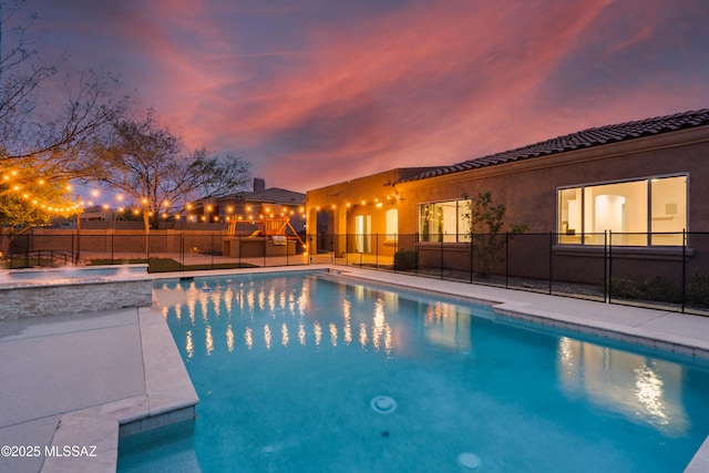 pool at dusk with a fenced in pool, fence, and an in ground hot tub