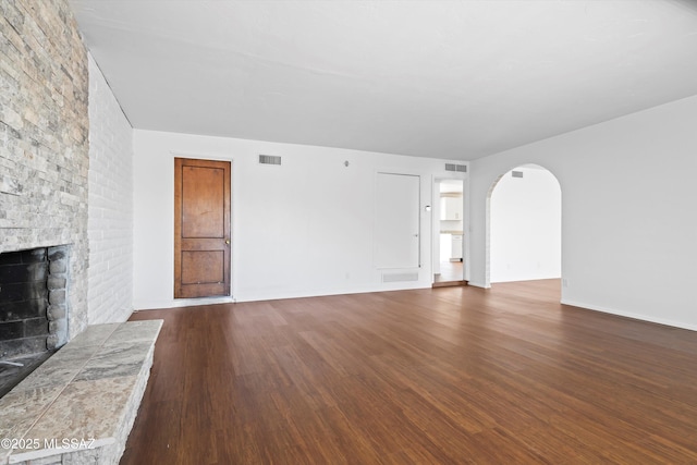 unfurnished living room with arched walkways, a brick fireplace, dark wood finished floors, and visible vents