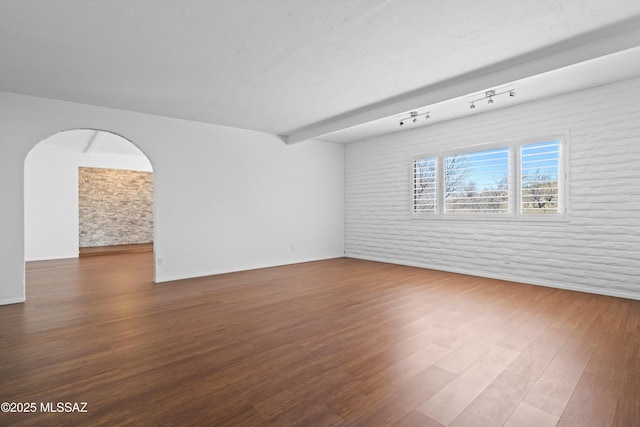 unfurnished room featuring arched walkways, brick wall, wood finished floors, and baseboards