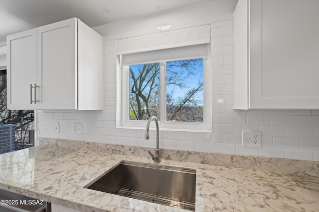 kitchen featuring light stone countertops, white cabinetry, backsplash, and a sink