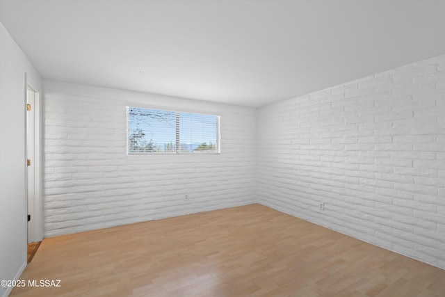 spare room featuring light wood-style floors and brick wall