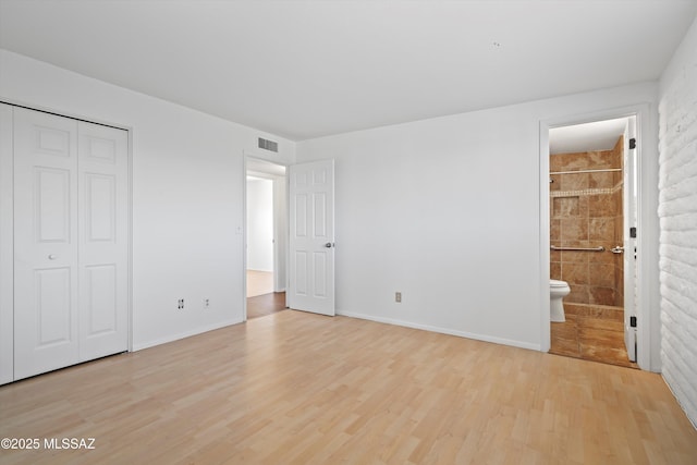 unfurnished bedroom featuring ensuite bath, light wood-style flooring, visible vents, and a closet