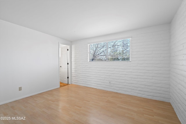 empty room featuring brick wall, wood finished floors, and baseboards