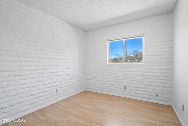 empty room with a textured ceiling, light wood finished floors, and baseboards