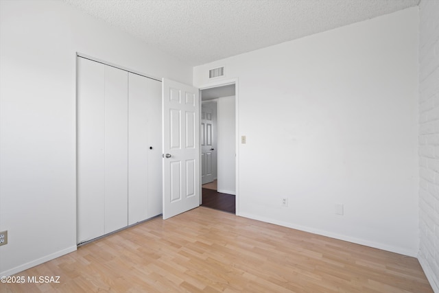 unfurnished bedroom featuring a textured ceiling, baseboards, visible vents, and light wood-style floors