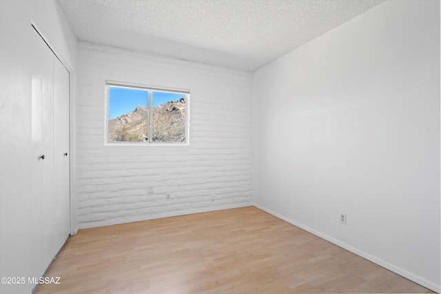 unfurnished bedroom featuring baseboards, brick wall, light wood-style flooring, a textured ceiling, and a closet