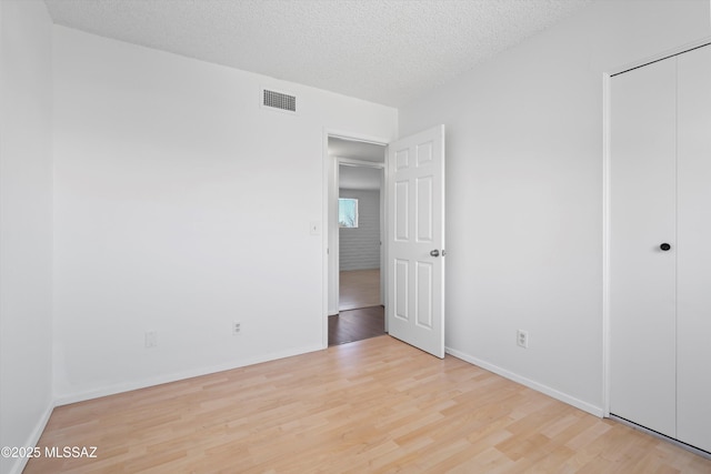 unfurnished bedroom featuring visible vents, a textured ceiling, baseboards, and wood finished floors