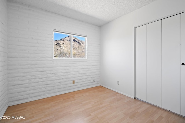 unfurnished bedroom featuring a textured ceiling, brick wall, a closet, and light wood-type flooring