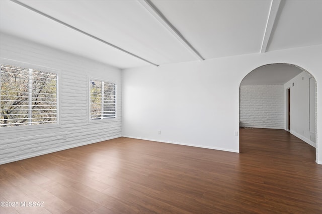 unfurnished room featuring beam ceiling, baseboards, brick wall, and wood finished floors