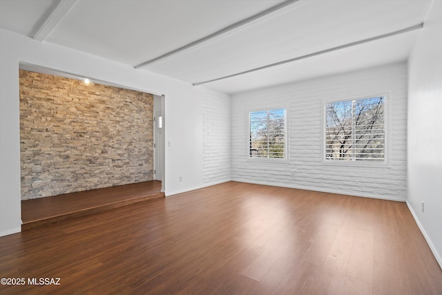 spare room with beam ceiling, baseboards, and wood finished floors