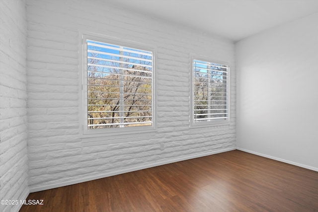 spare room featuring brick wall, wood finished floors, and baseboards