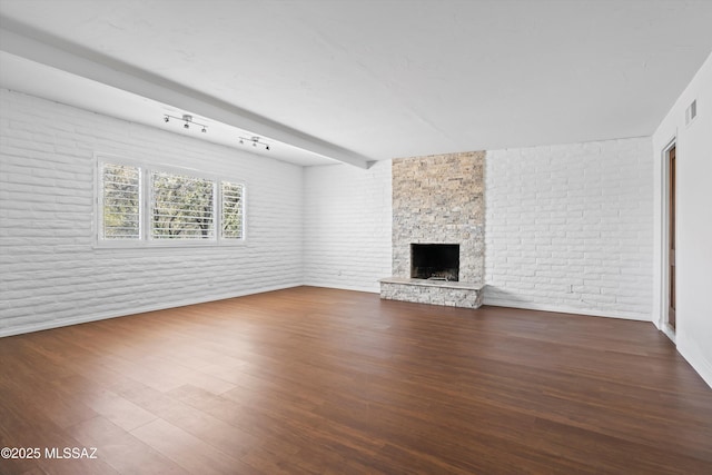 unfurnished living room with brick wall, a stone fireplace, and wood finished floors