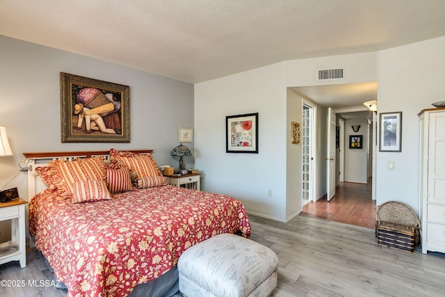 bedroom featuring visible vents, a textured ceiling, baseboards, and wood finished floors