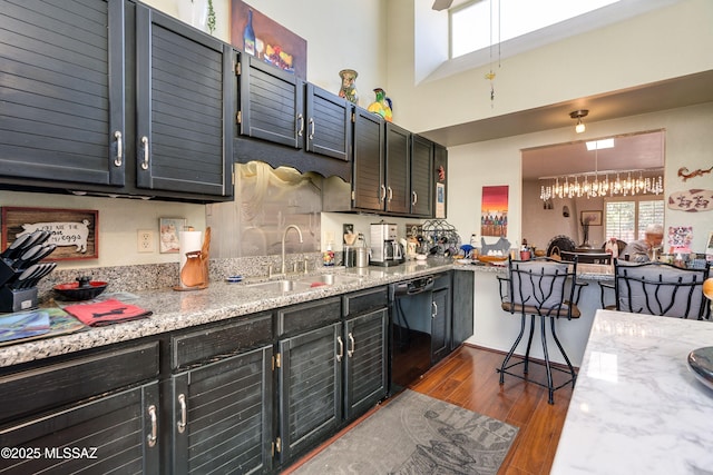 kitchen featuring light stone counters, dark wood-style flooring, a towering ceiling, a sink, and dishwasher