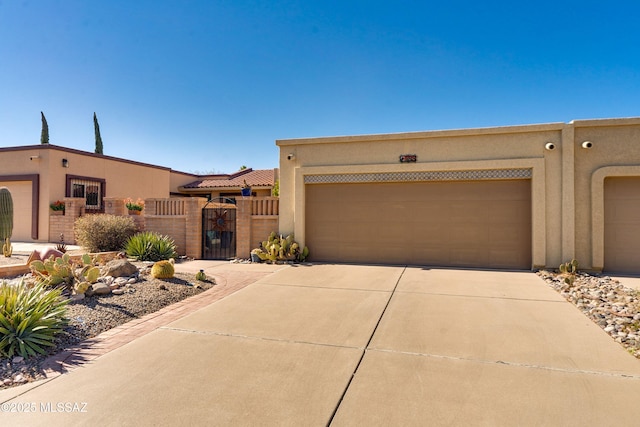 pueblo-style house featuring concrete driveway, fence, a gate, and stucco siding