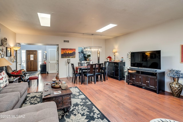 living area with light wood-style floors, a skylight, visible vents, and a chandelier