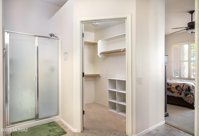 ensuite bathroom with a spacious closet, a ceiling fan, connected bathroom, a shower stall, and baseboards