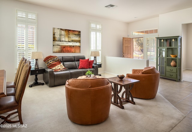 carpeted living area with a healthy amount of sunlight, visible vents, baseboards, and tile patterned floors