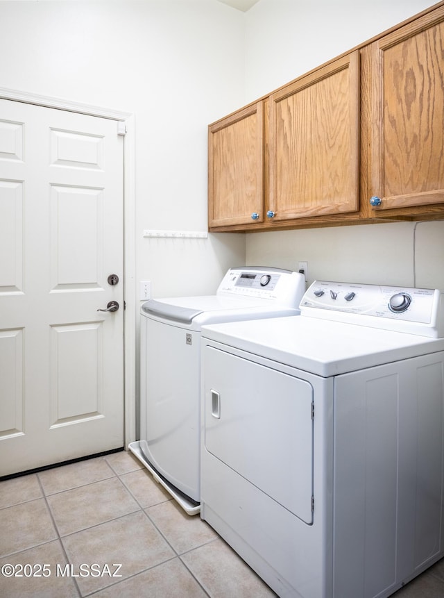 clothes washing area with cabinet space, light tile patterned floors, and washing machine and clothes dryer