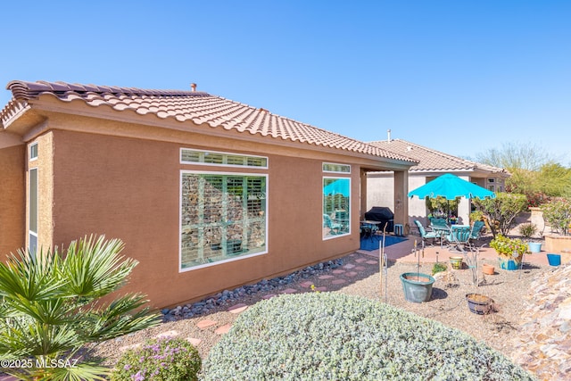 view of property exterior featuring a tile roof, a patio area, and stucco siding