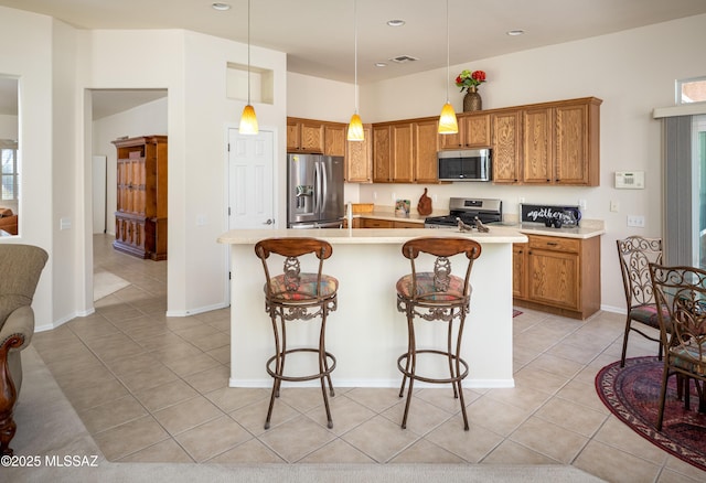 kitchen with light tile patterned floors, a breakfast bar, light countertops, appliances with stainless steel finishes, and brown cabinetry