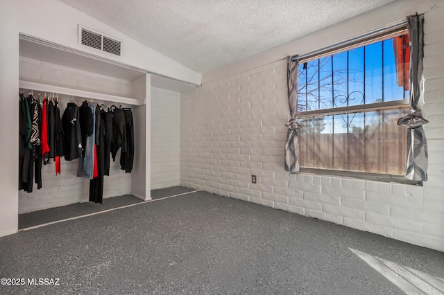 spare room featuring a textured ceiling, speckled floor, visible vents, and concrete block wall