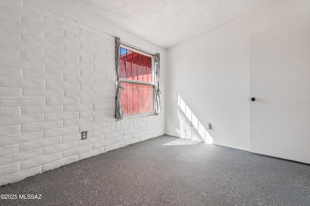 unfurnished room with concrete block wall, a textured ceiling, and speckled floor