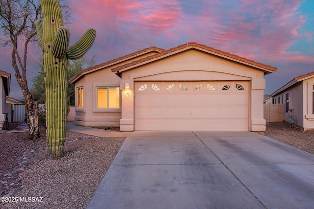 view of front of home featuring concrete driveway, a tiled roof, an attached garage, and stucco siding