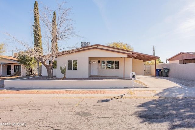 view of front facade with an attached carport, driveway, fence, and stucco siding