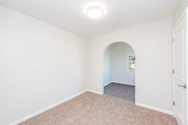 spare room featuring arched walkways, carpet flooring, and baseboards