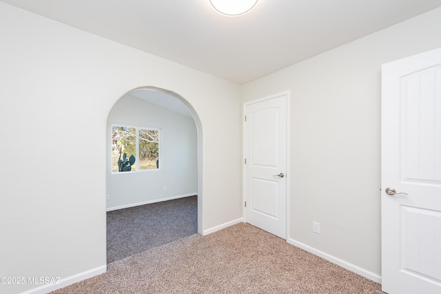 unfurnished room with carpet, baseboards, and arched walkways