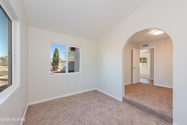 spare room featuring light carpet, baseboards, visible vents, arched walkways, and vaulted ceiling