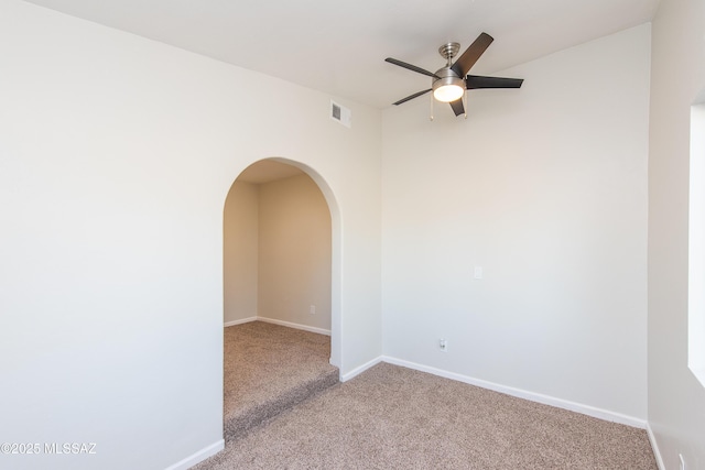 empty room featuring arched walkways, carpet, visible vents, a ceiling fan, and baseboards